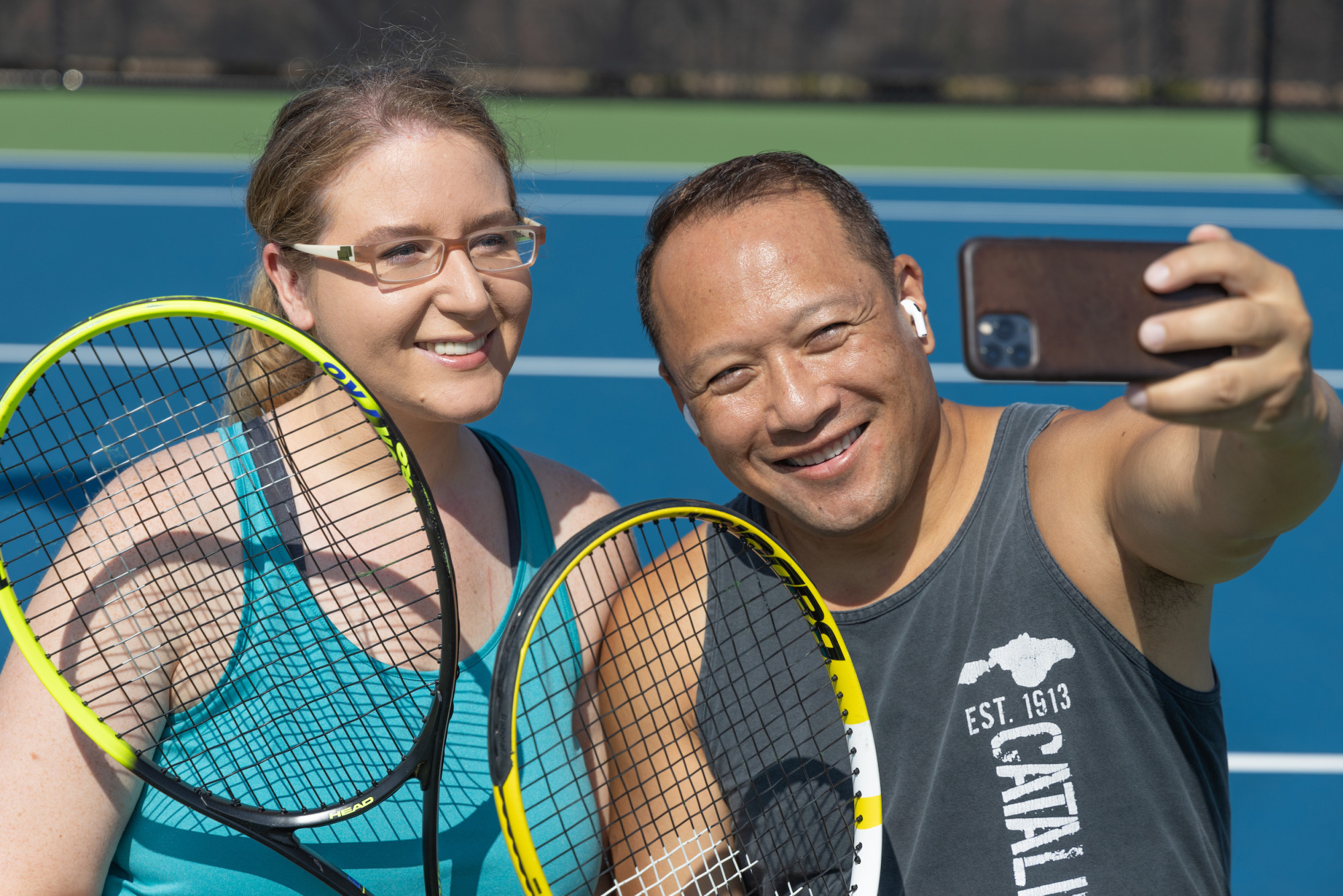People taking a selfie at a tennis court with their rackets