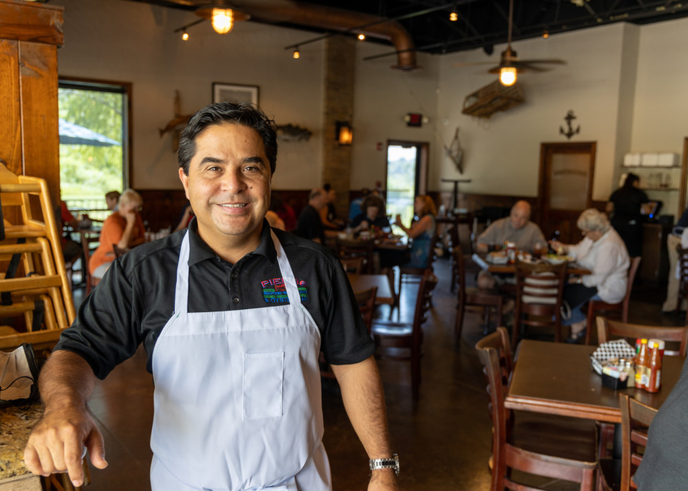 Worker at a restaurant smiling with guests in the background